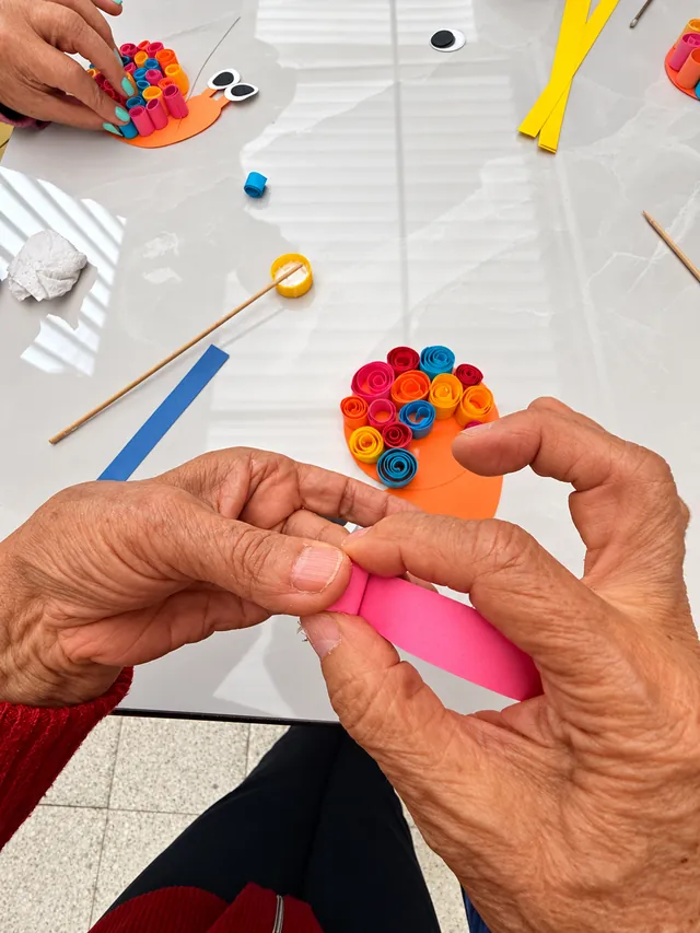Manos enrollan tiras de papel de colores para crear caracoles en un taller de arteterapia