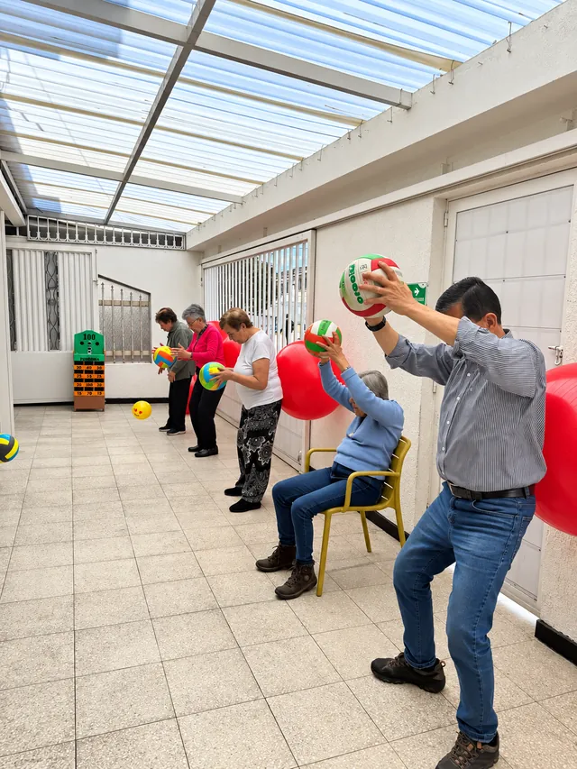 Personas mayores realizan ejercicios en grupo con pelotas, de pie y sentadas