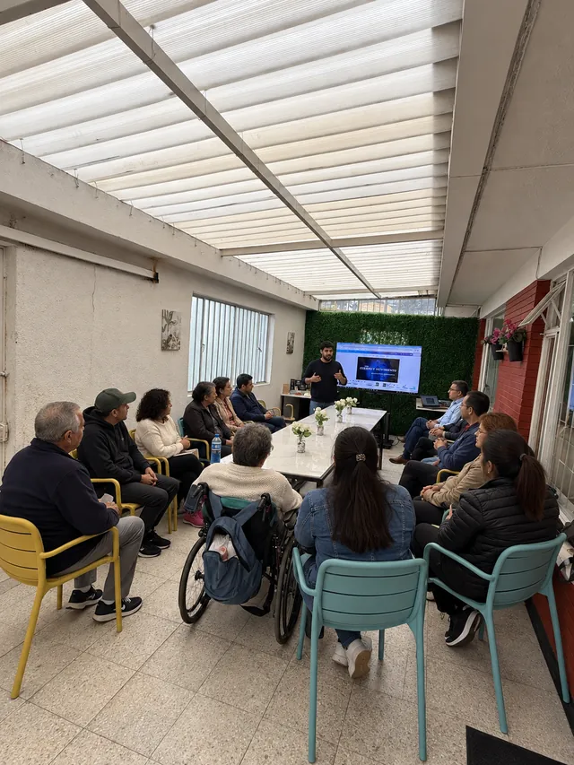 Grupo de personas participa en una charla alrededor de una mesa con un expositor
